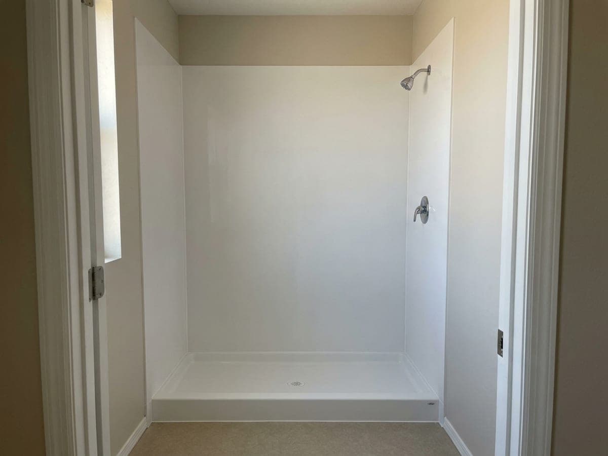 A plain alcove shower with a white shower pan, smooth white wall panels, a chrome showerhead and a single-handle valve, with no door